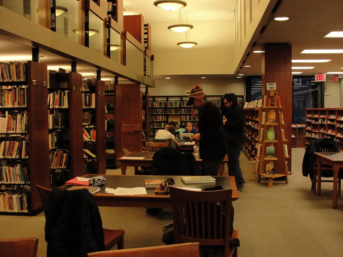 people, desks, and shelves in a warm and wooden library